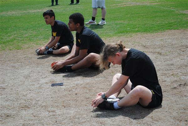 three students sitting on the ground stretching