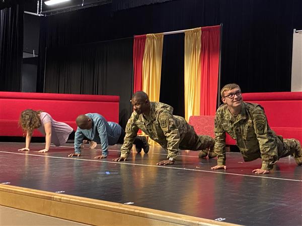 four students doing pushups on stage