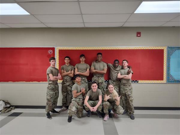 nine JROTC students pose in front of a bulletin board