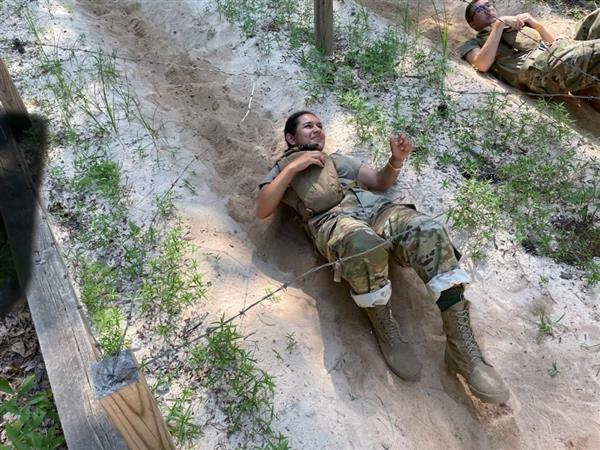 students slide on their backs under barbed wire