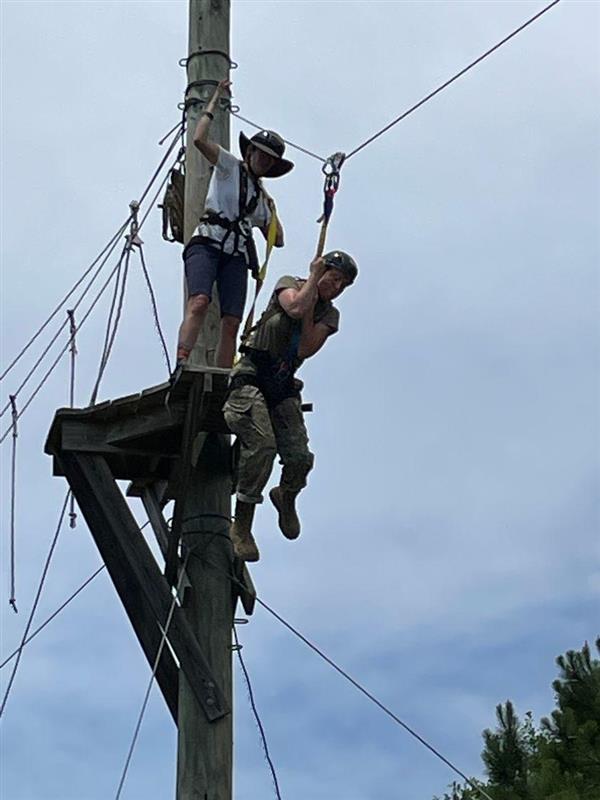 student takes off on a zipline while another person stands on the platform behind them