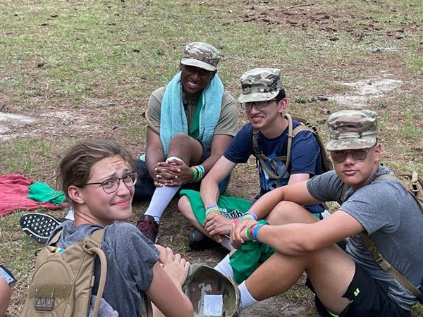 four students sitting on the ground smile for the camera