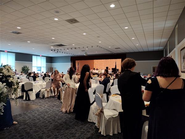 people standing in a big room decorated with flowers and filled with tables