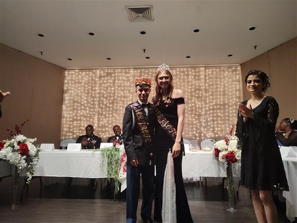 two students wearing crowns and sashes smile for the camera