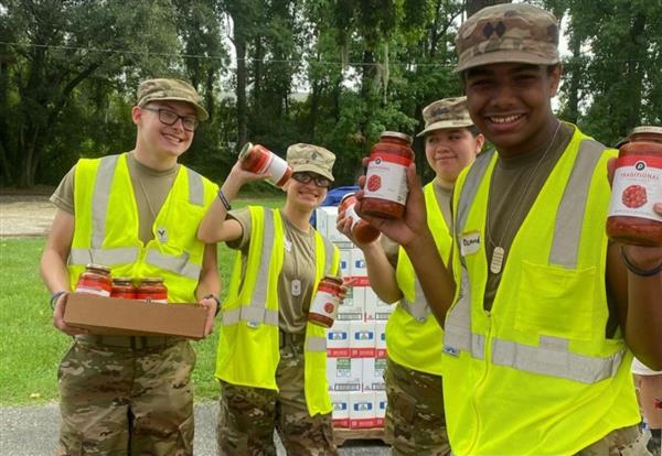 four students wearing safety vests and holding jars of pasta sauce