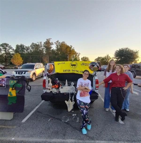 four student stand next to a pickup truck decorated for halloween with a JROTC banner