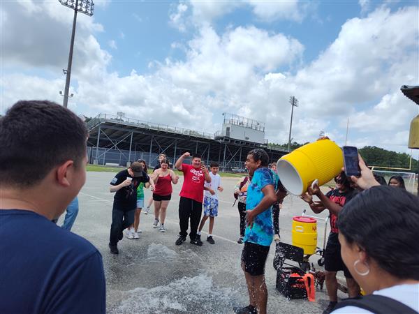 a group stands around. The person in the center has just had a large container of ice water poured on them