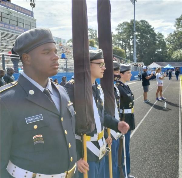 four students stand at attention holding flags