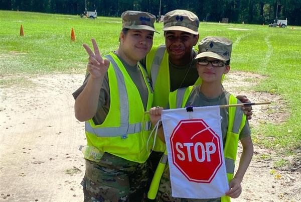 three students wearing safety vests and holding a flag with a stop sign on it