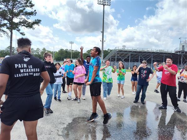 a group stands around. The person in the center is reacting to having large container of ice water poured on them