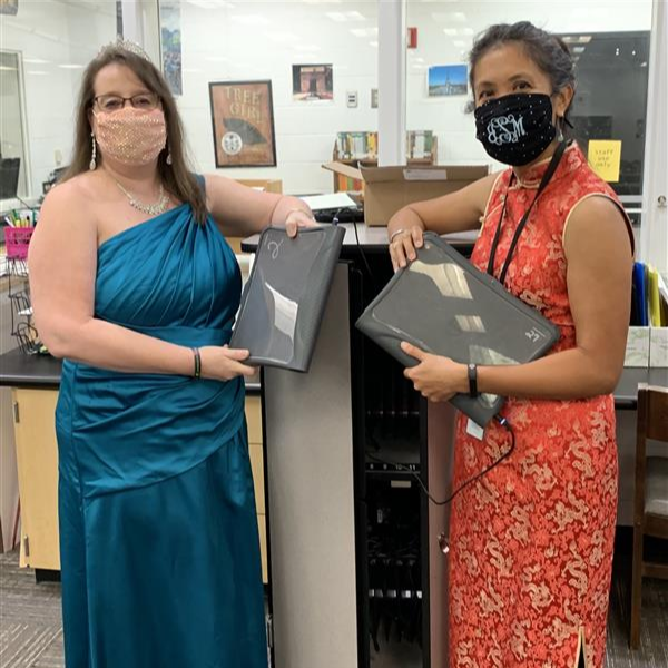 Two people stand in the media center holding chromebooks