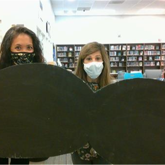 Three people hold up a giant moustache cutout