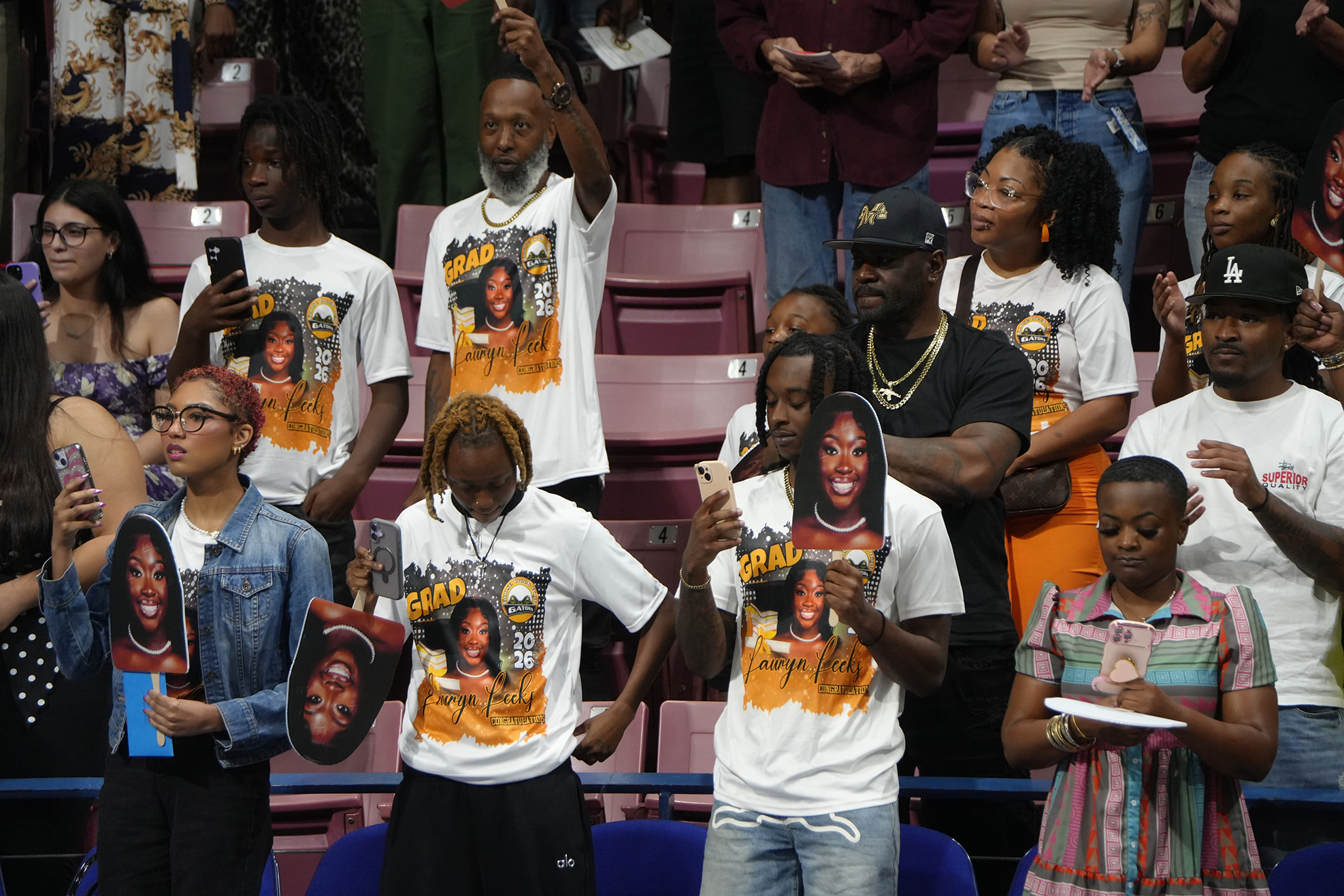 A group of people in a stadium, some holding signs, wearing white t-shirts with printed images.