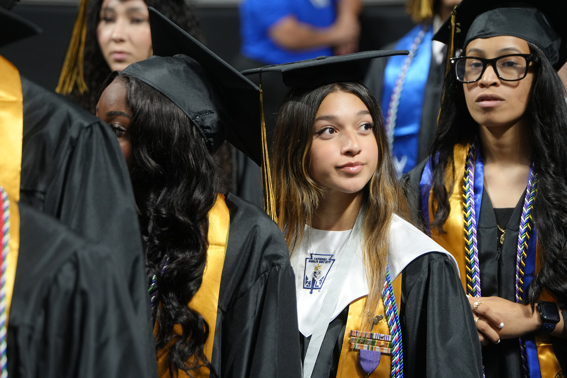 A row of students wearing graduation gowns and caps. One student wears a medal.
