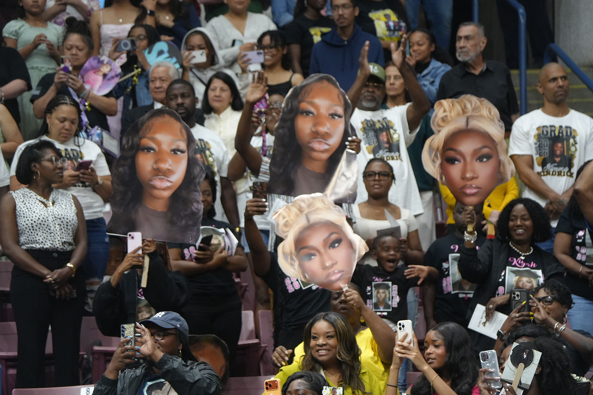 Audience members at a sports event hold up large cutouts of women's faces during a break.