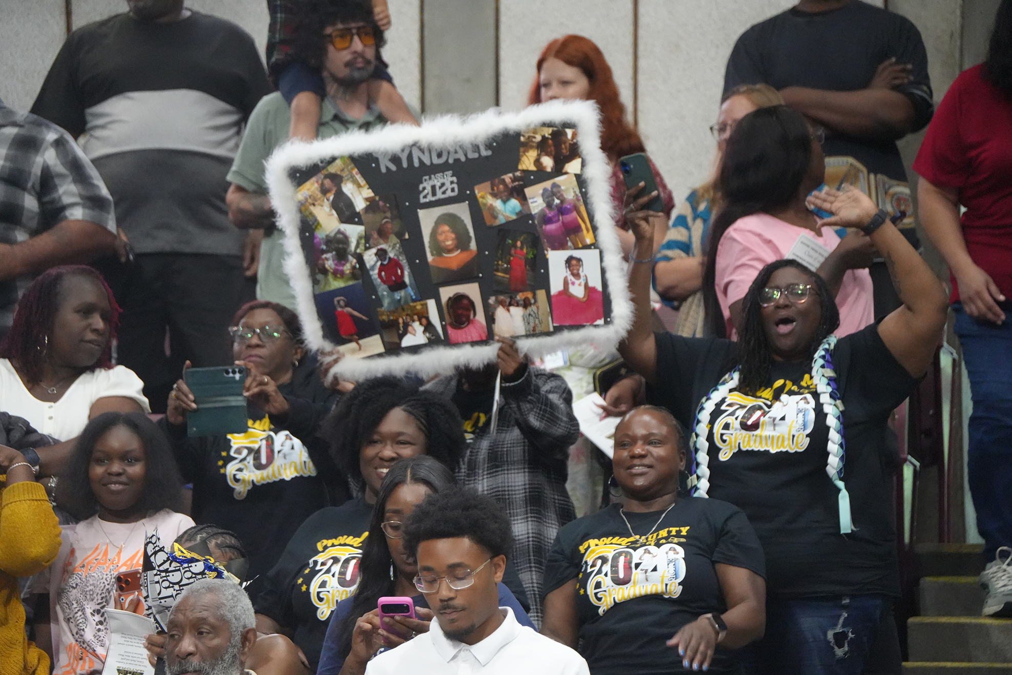 A group of people in black shirts and glasses standing and holding a collage photo in a stadium.