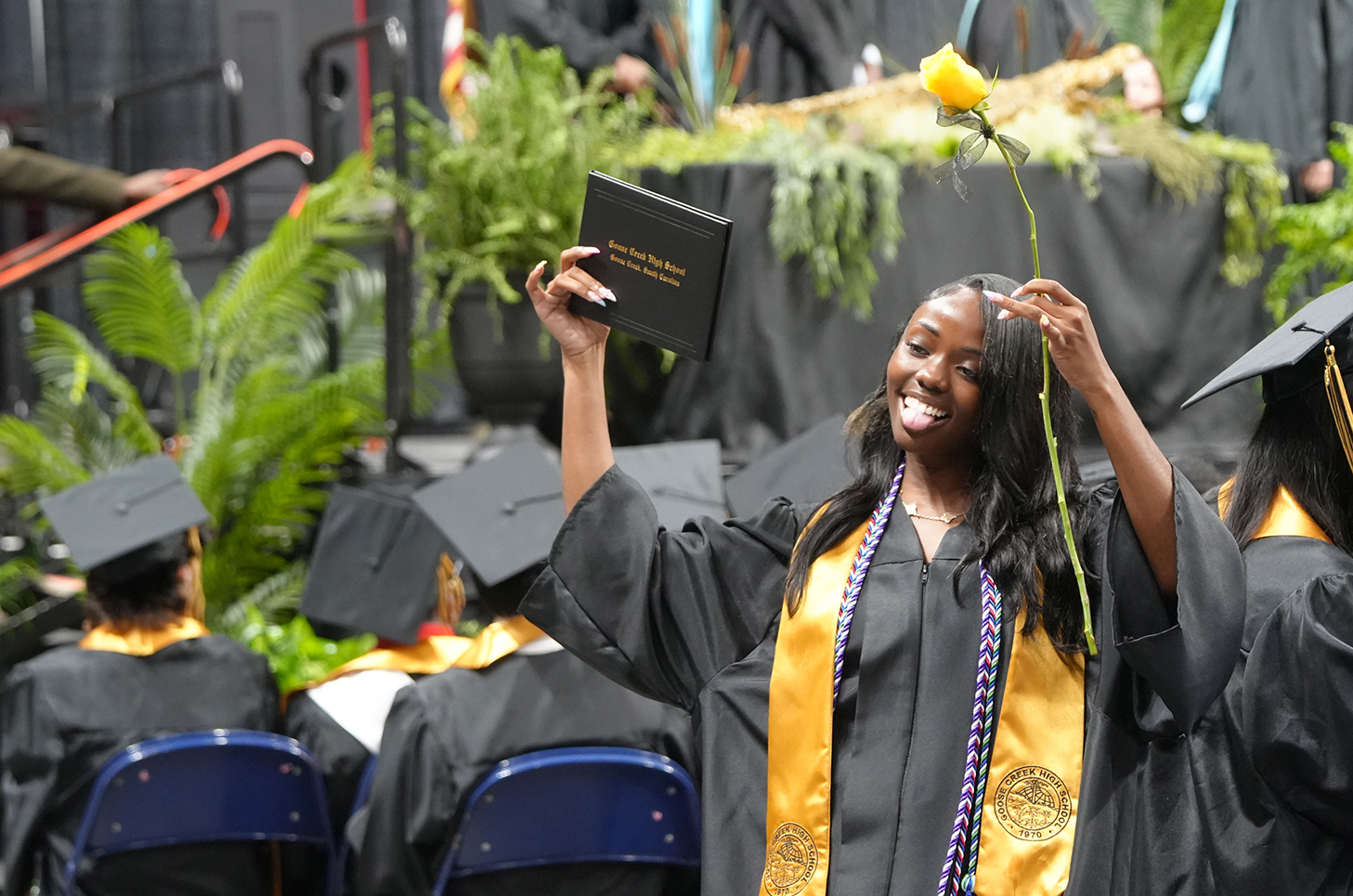A woman in a cap and gown holds her diploma over her head during a graduation.