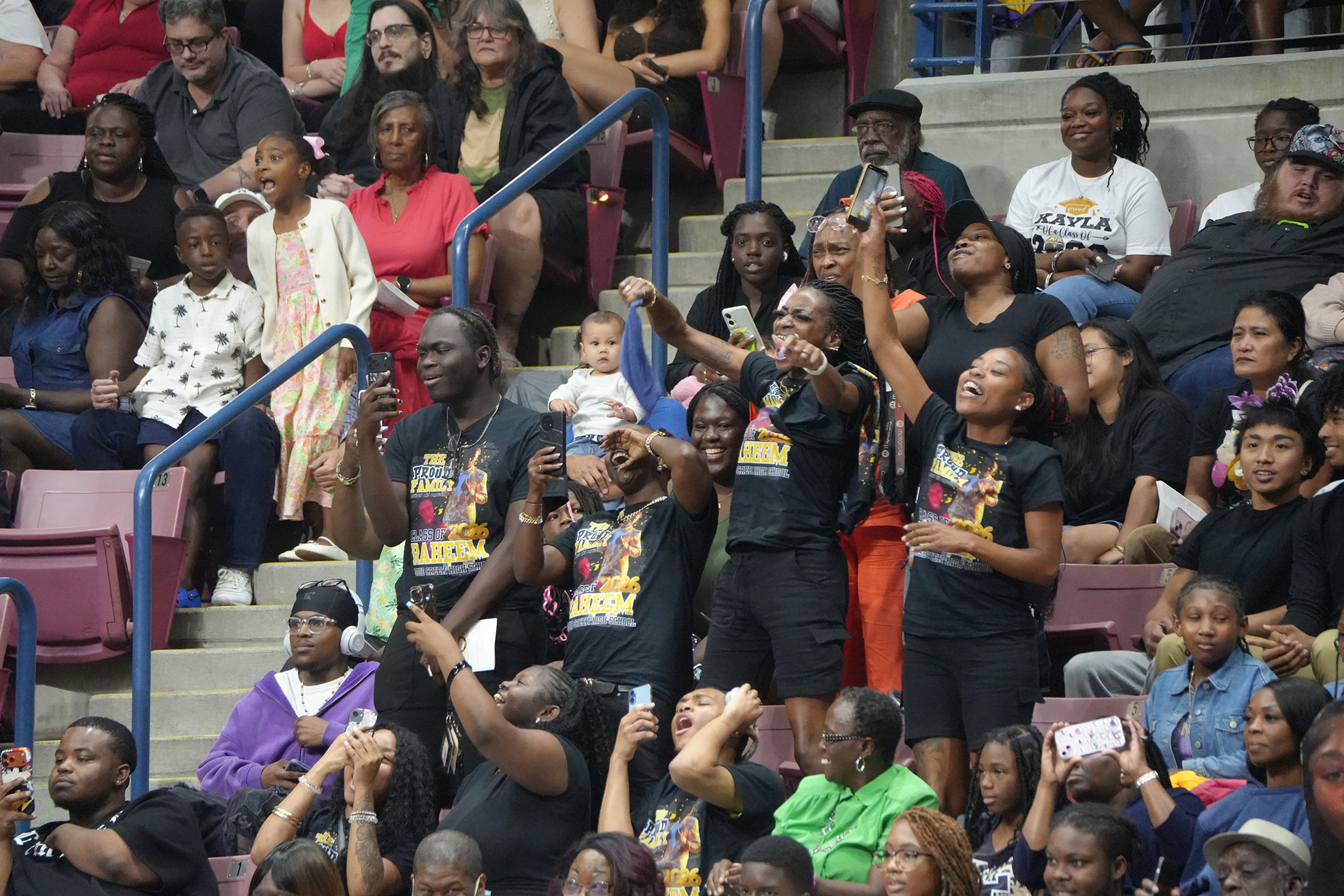 A diverse group of people seated in bleachers, some with hands raised, watching an event.