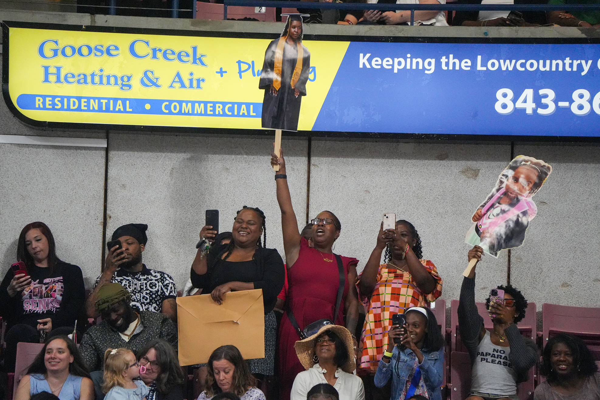 Several people hold signs and dolls in a stadium with a banner for Goose Creek Heating & Air.
