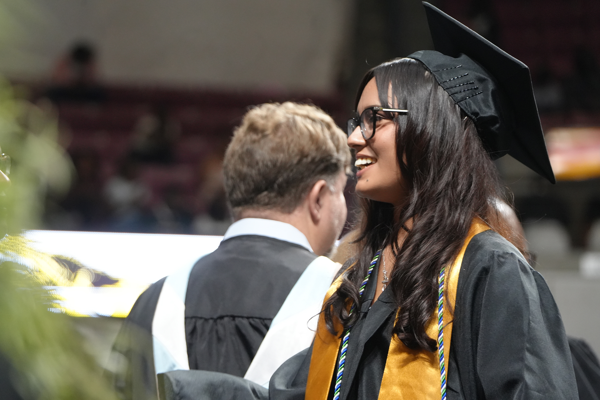 A woman in a cap and gown smiles at a man in front of her. They are seated at an event.