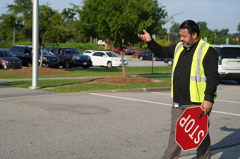 Person in high-visibility clothing directs traffic with a red sign that reads "STOP" in a parking lot.