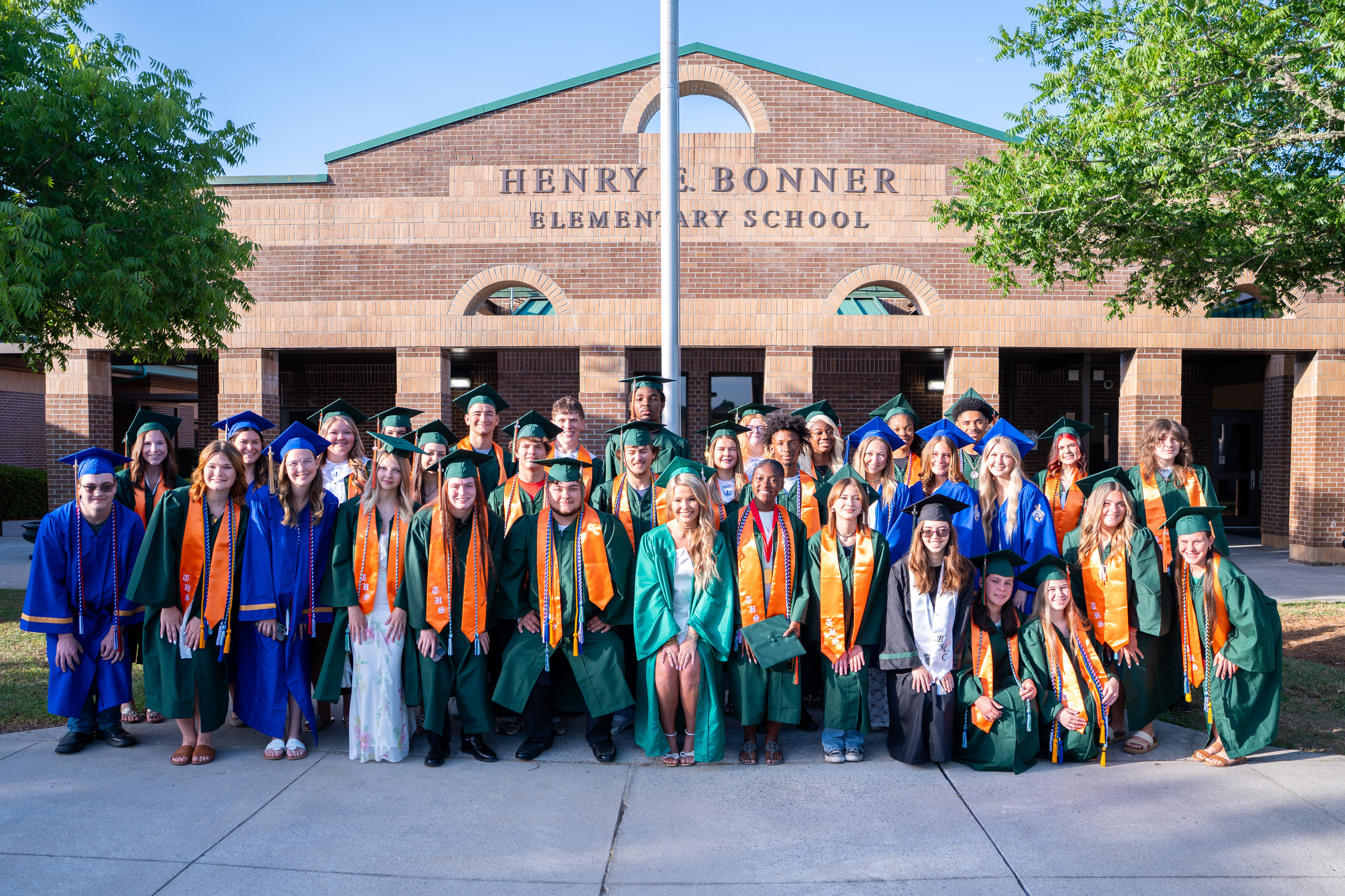 A group of people in caps and gowns pose for a photo outside a school building.