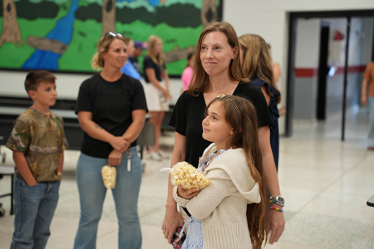 Four adults and two children in a hallway with a mural of a river and trees in the background.