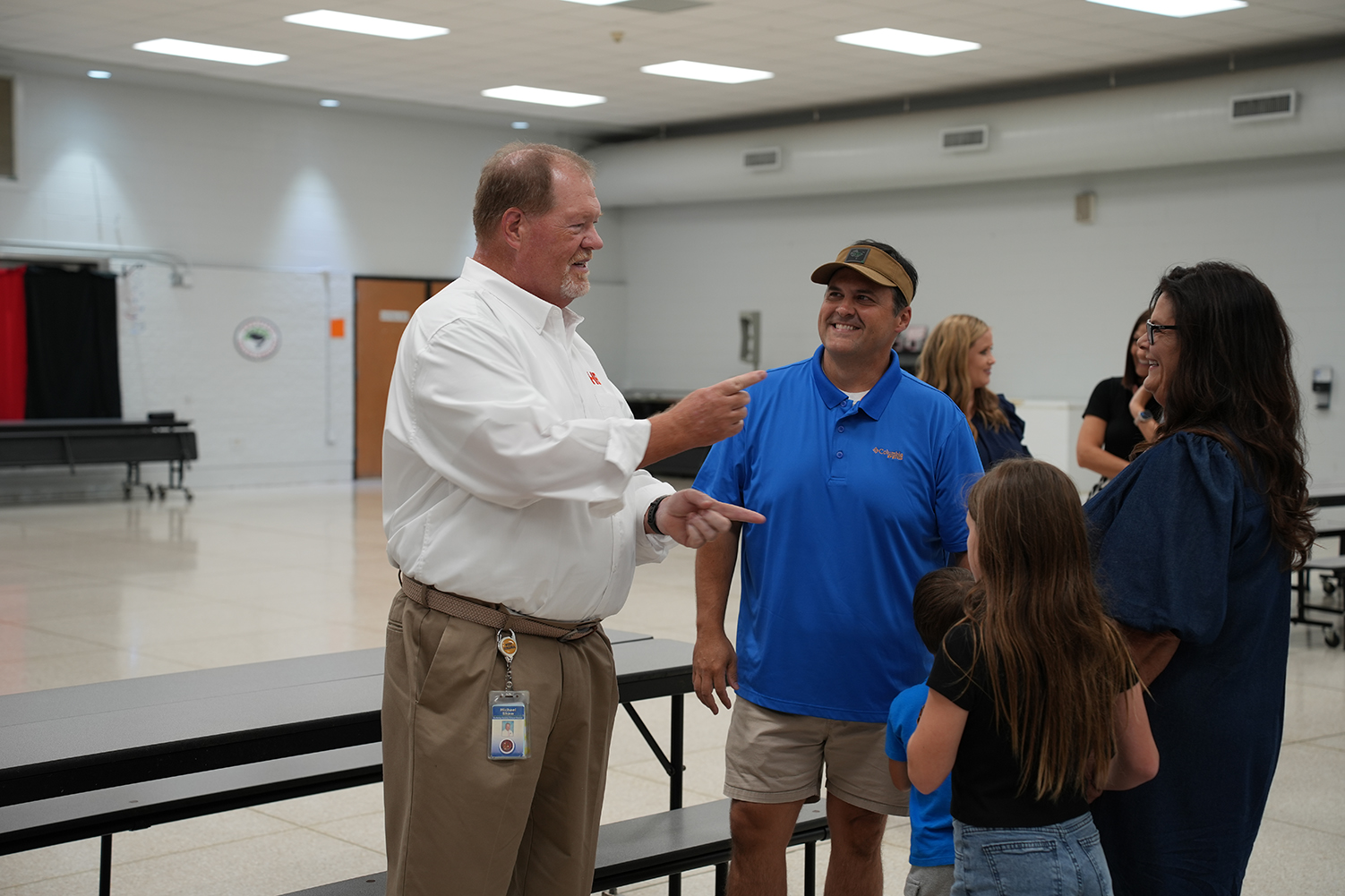 People standing in a room with white walls, a person pointing at another, and a group of people nearby.