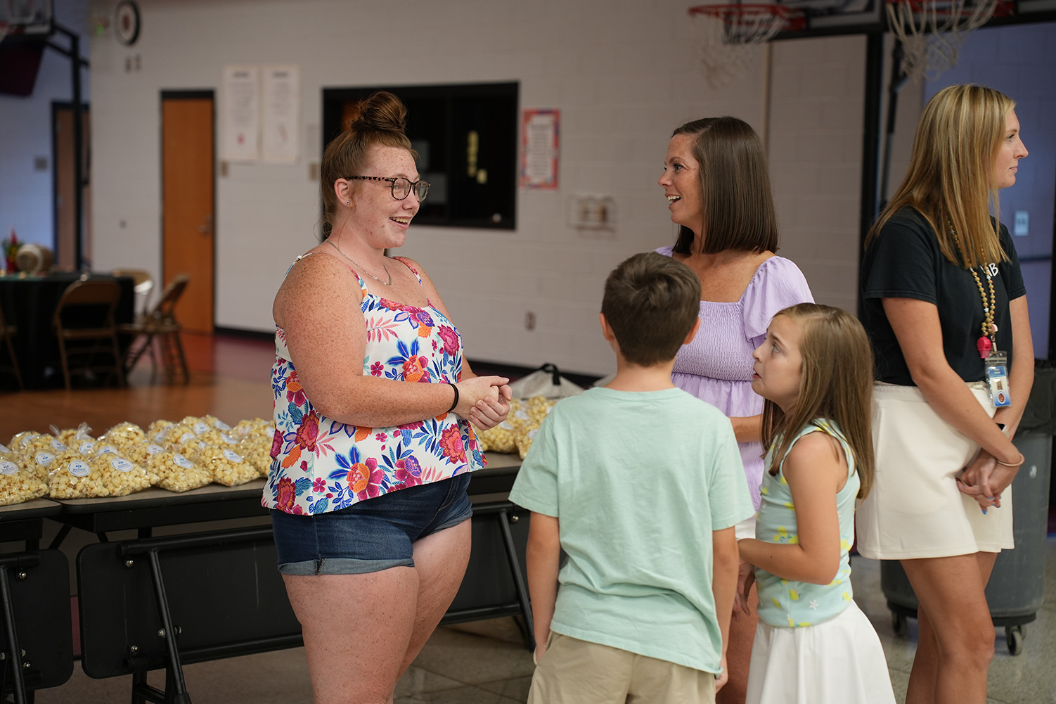 Five people in a gym, including a woman with glasses, two children, and two women with long hair.