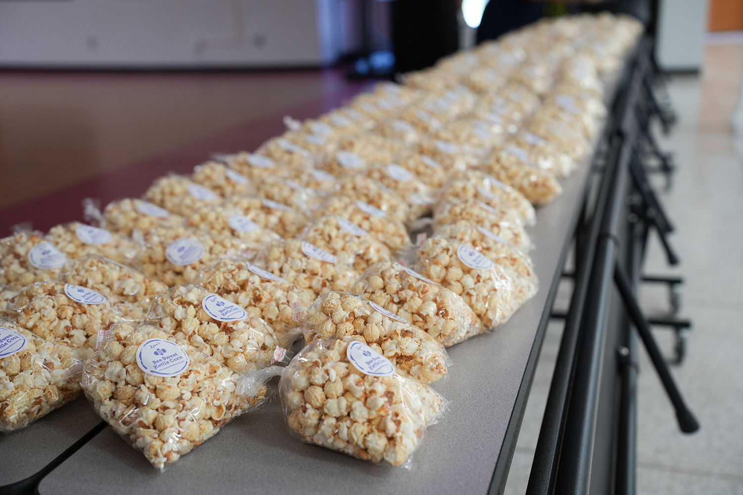 Many rows of popcorn bags in plastic, arranged on a table in a room with a tiled floor.