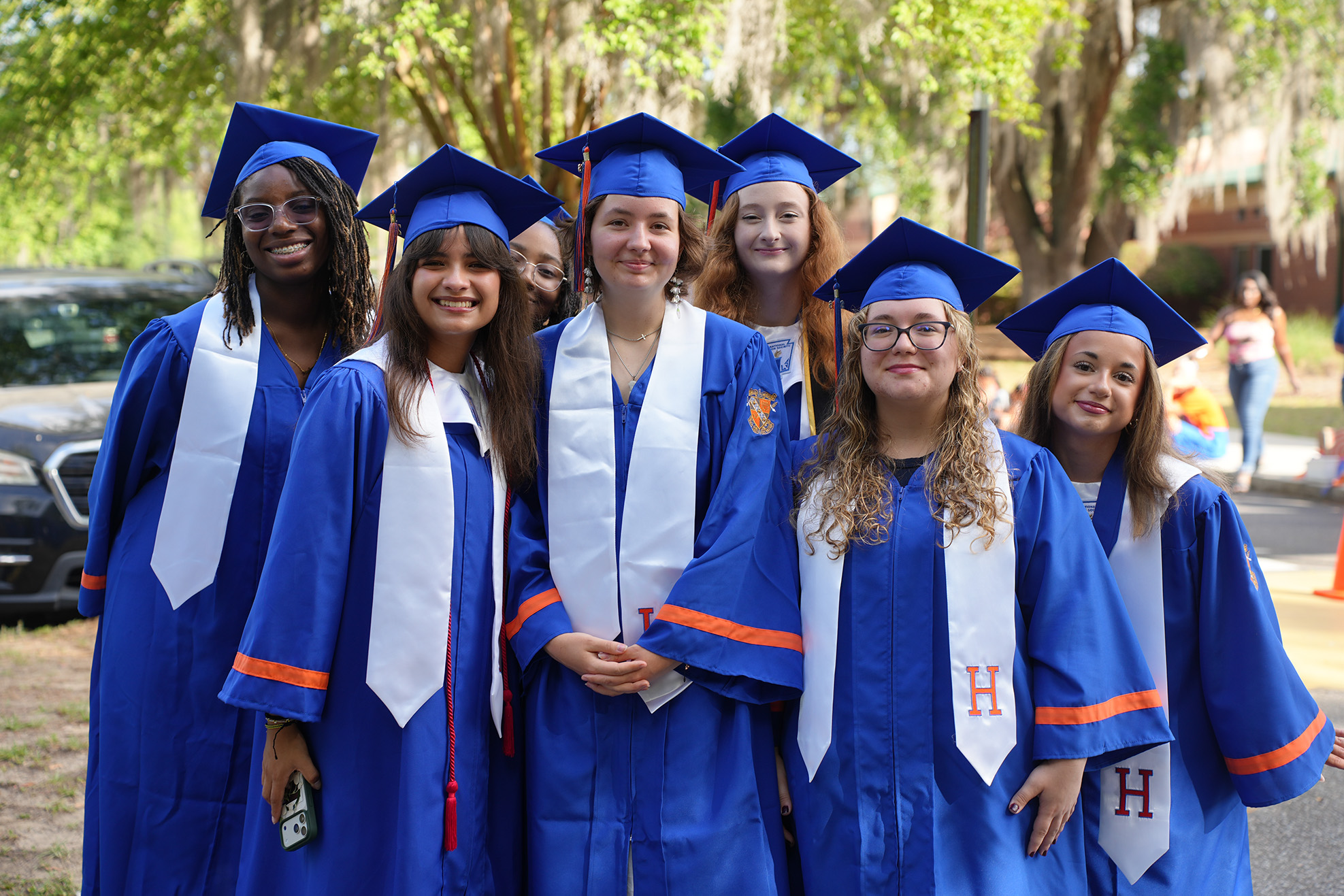 A group of young women in blue graduation gowns and caps pose for a photo outdoors.