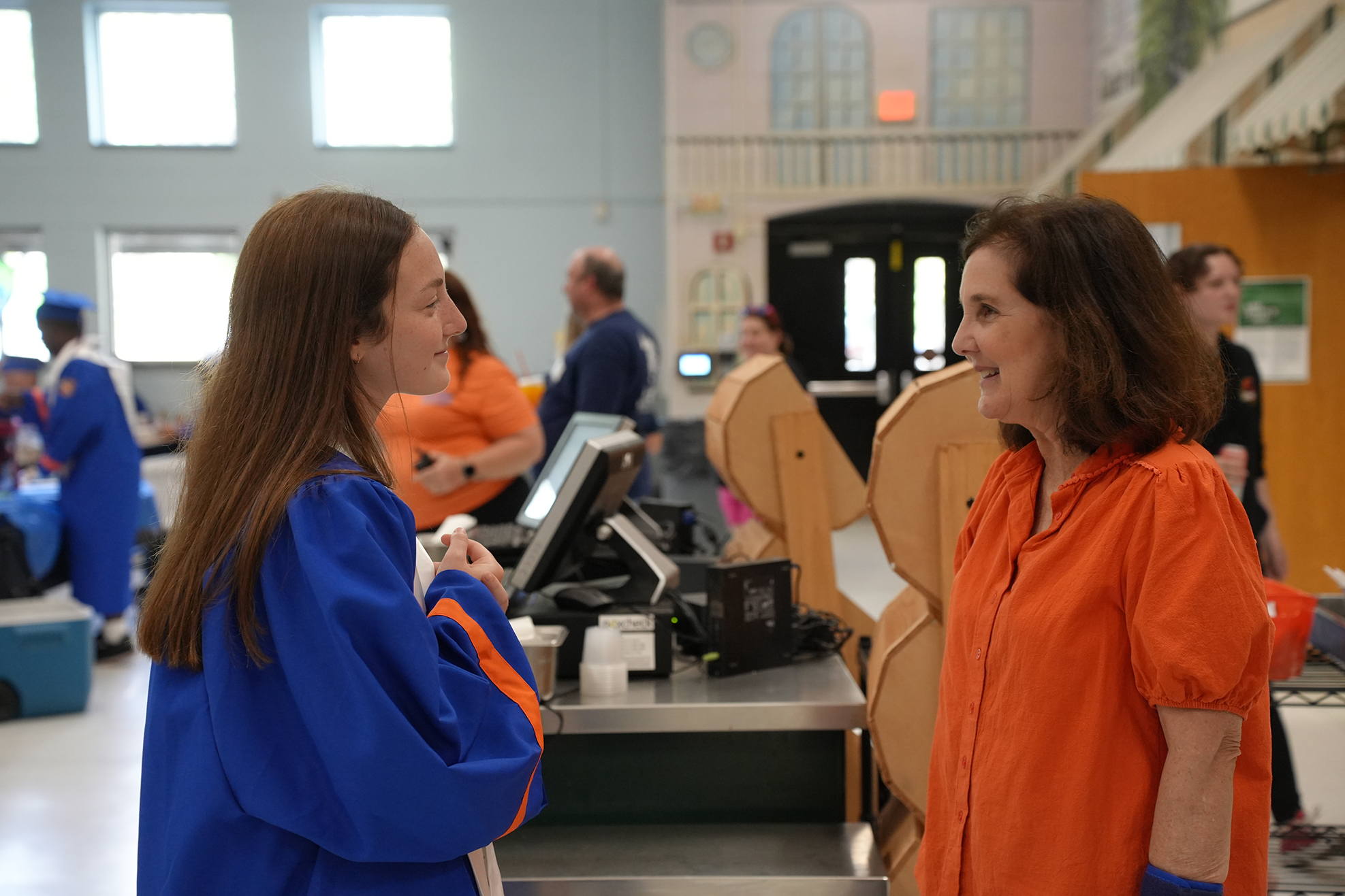 Two women face each other in a room, one wearing a blue robe and the other an orange shirt.