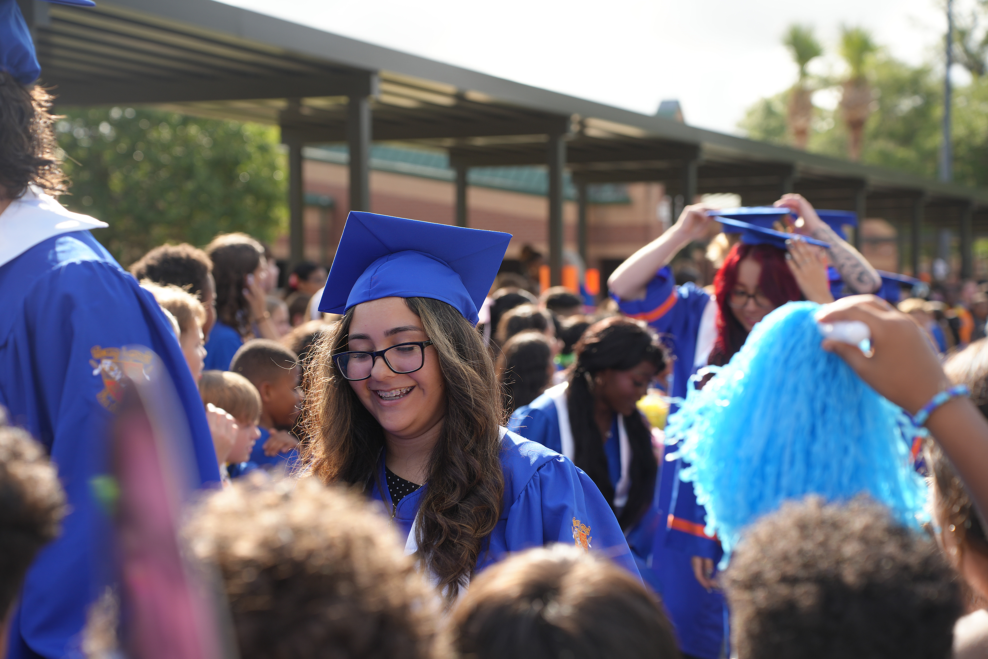 Several people in blue graduation gowns and caps, gathered outdoors. A woman smiles and stands in the foreground.