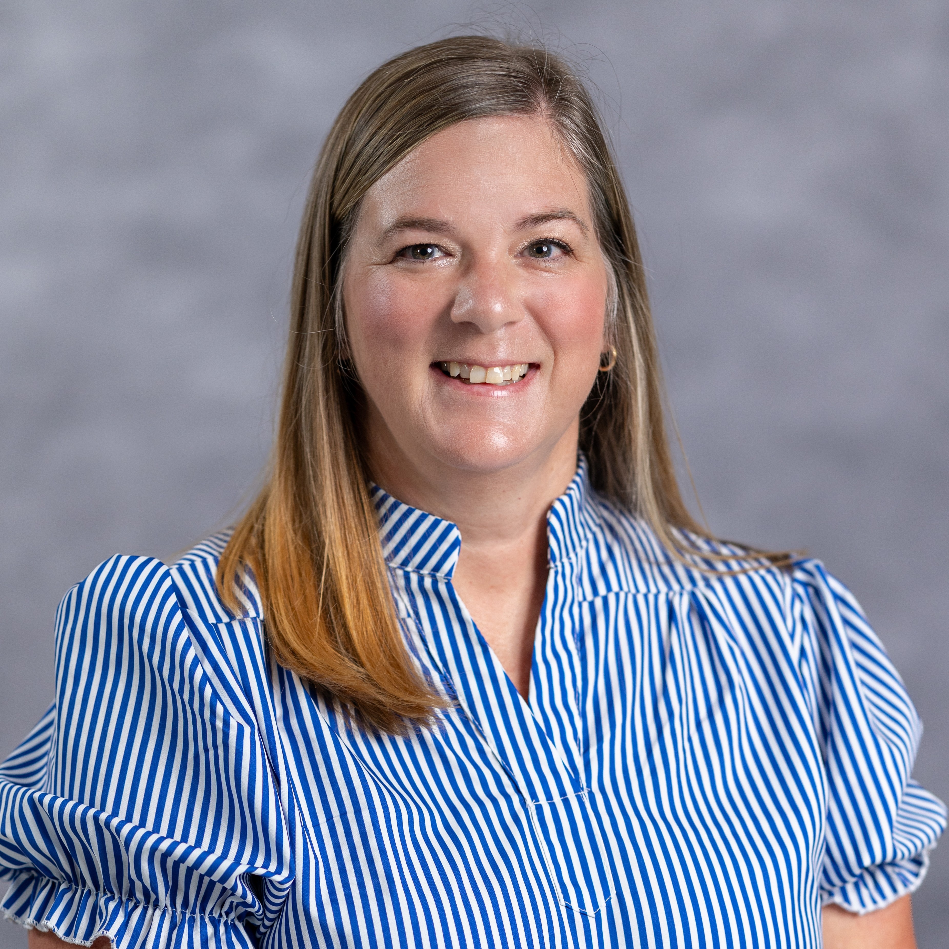 A woman with blonde hair wears a blue and white striped shirt with puffed sleeves. She smiles at the camera.