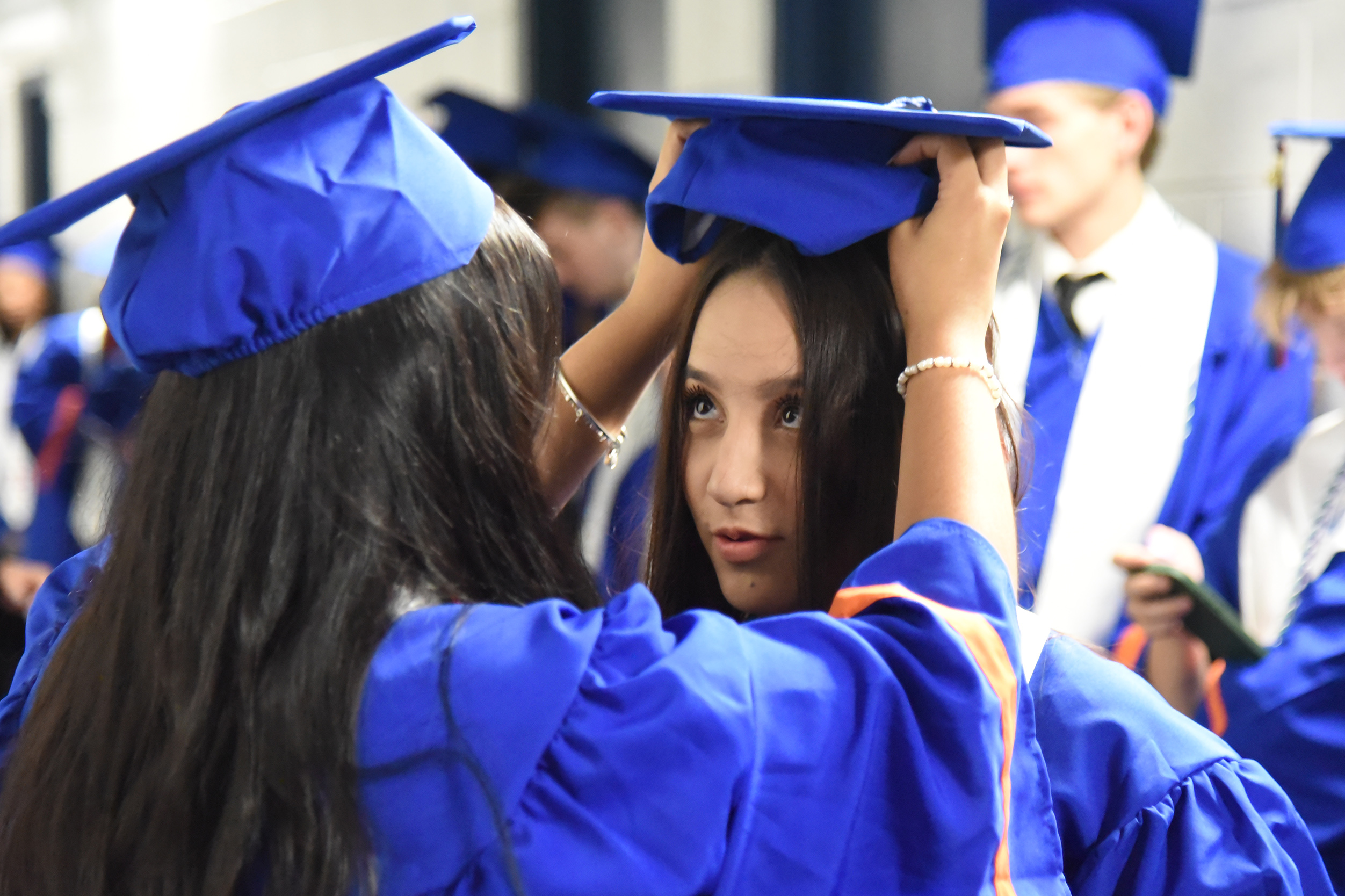 People in blue caps and gowns. One woman holds another's cap over her head.