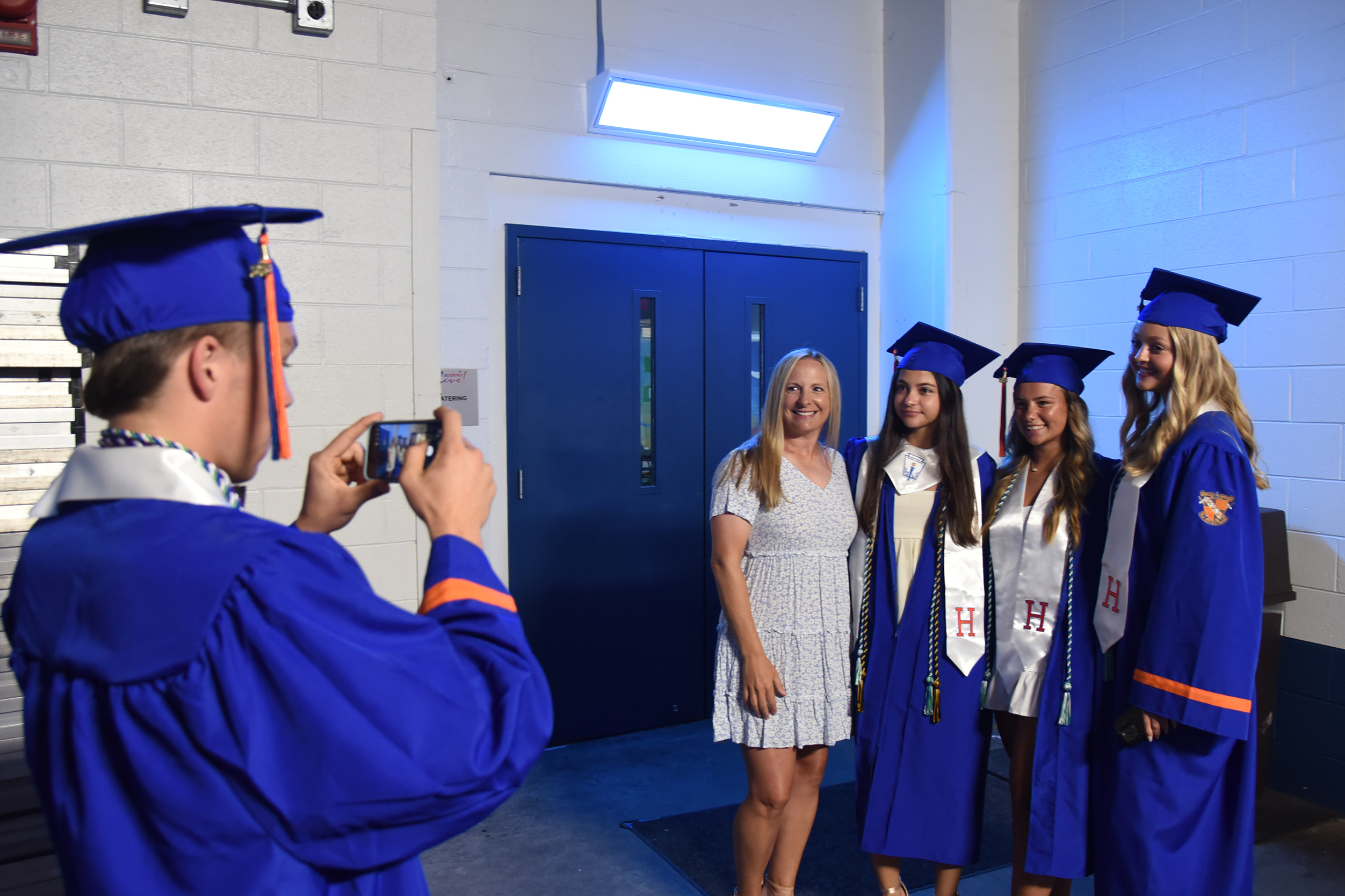 A man in a cap and gown takes a picture of four women in gowns and caps.