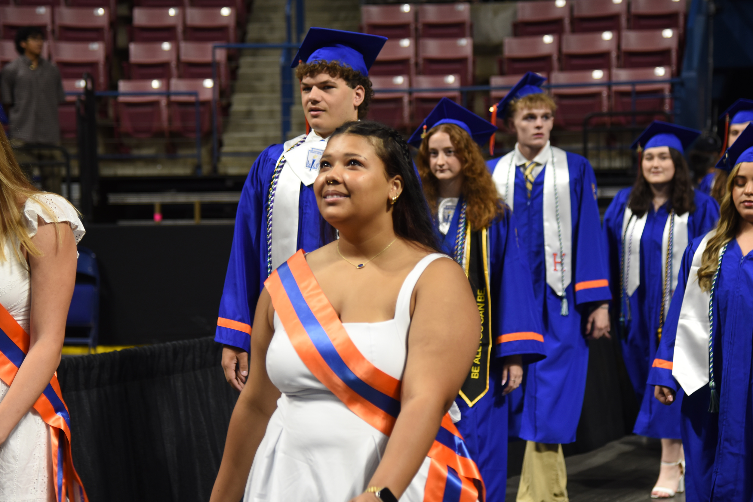 A group of people in caps and gowns, smiling, walk in a line at an event.