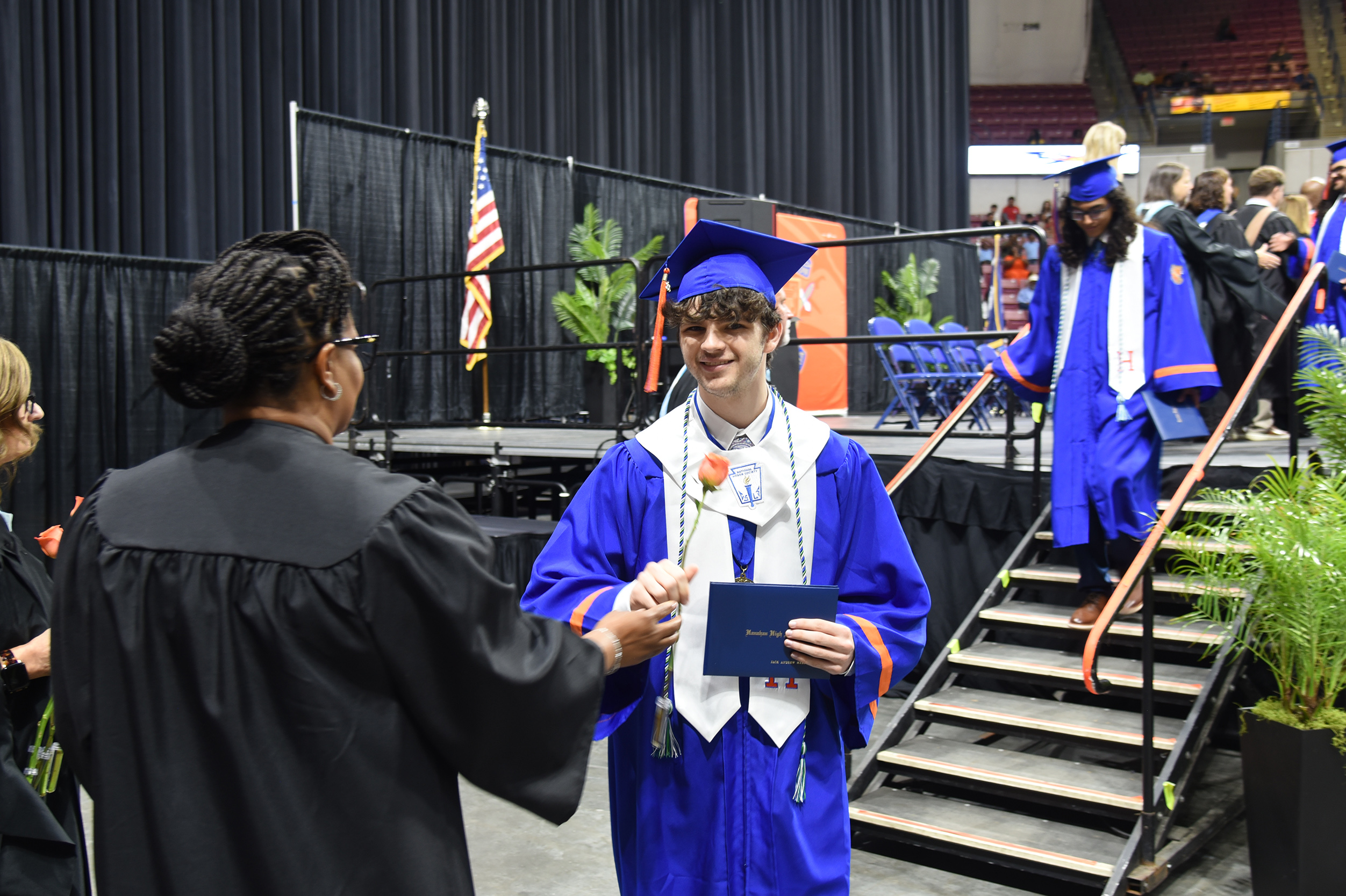 A person in a black gown hands a diploma to a person in a blue cap and gown.