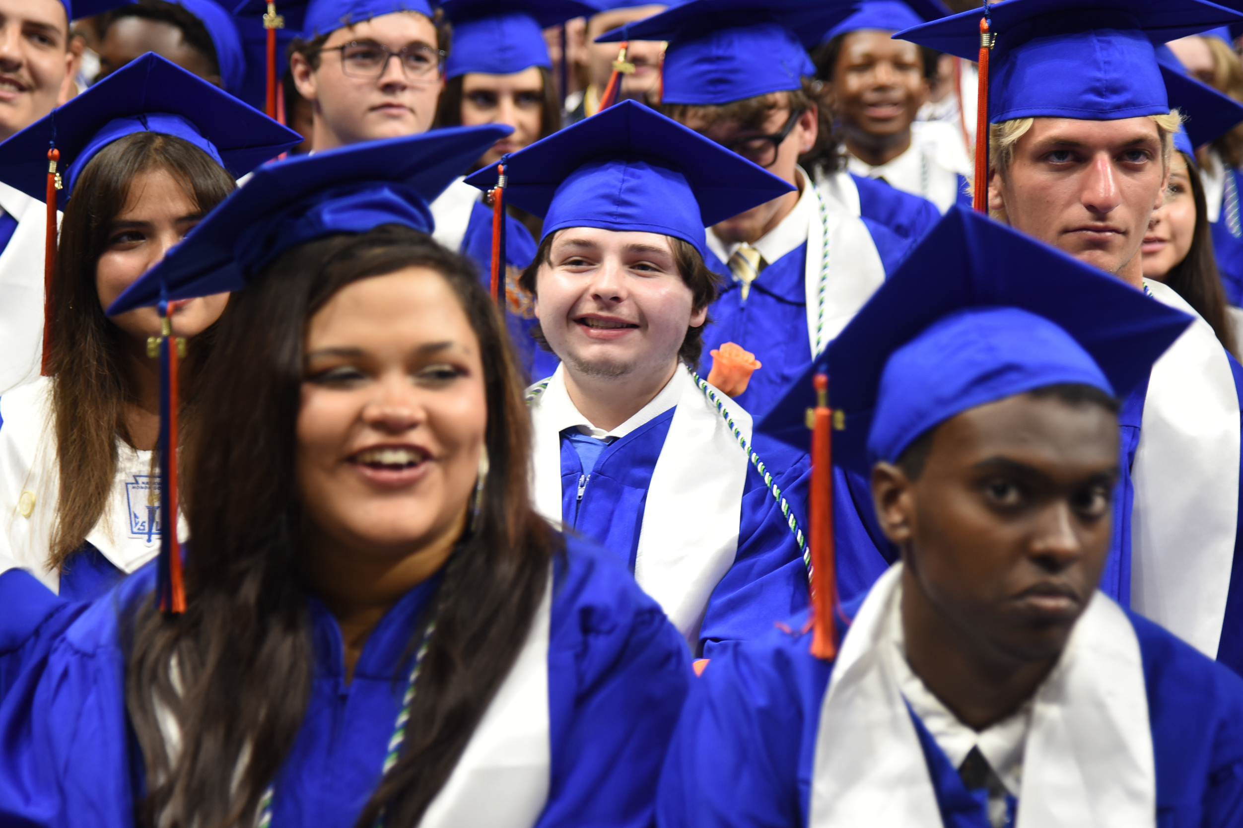 A crowd of graduates in blue gowns and caps, some smiling and others focused on the camera.