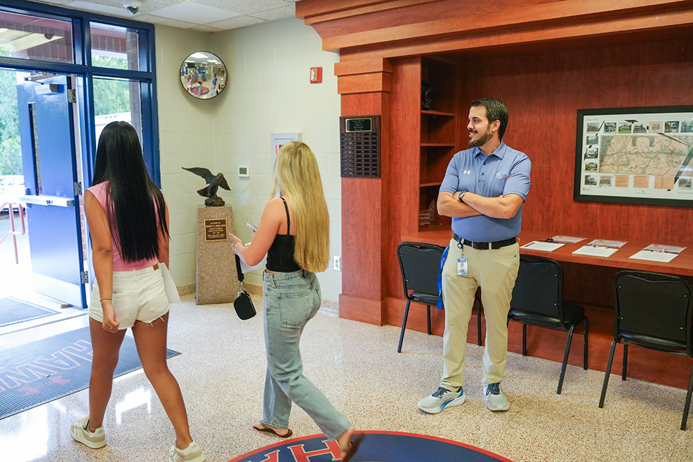 Four people in a lobby. A man with his arms crossed, and three women with their backs to the camera.