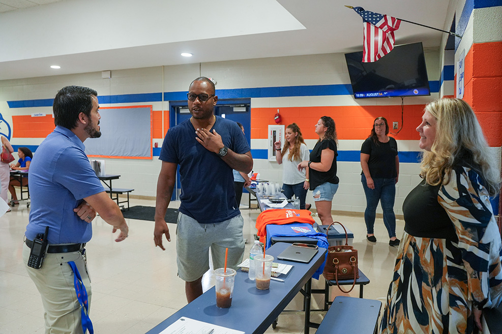 Several people standing around a table in a room with a US flag on the wall.