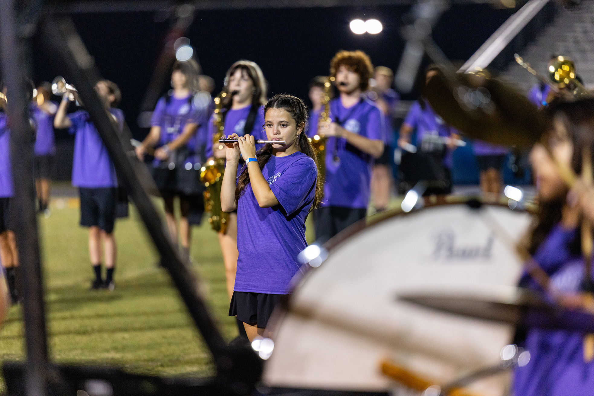 A group of children in purple uniforms performs on instruments on a grassy field at night.