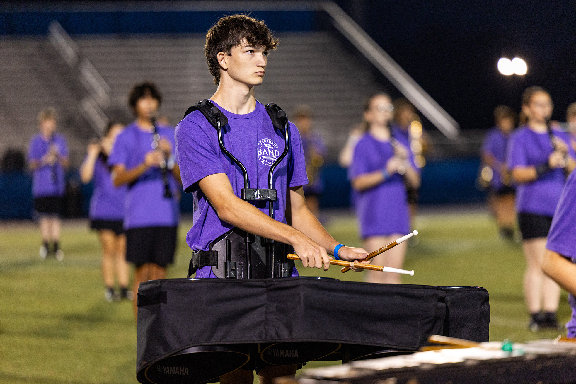 Musicians in purple uniforms on a field. A man holds xylophone mallets and a xylophone in front.