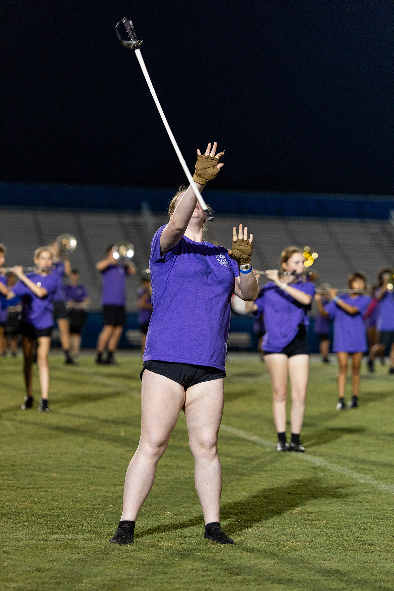 A person in purple with black shorts holds a baton above their head in a stadium.
