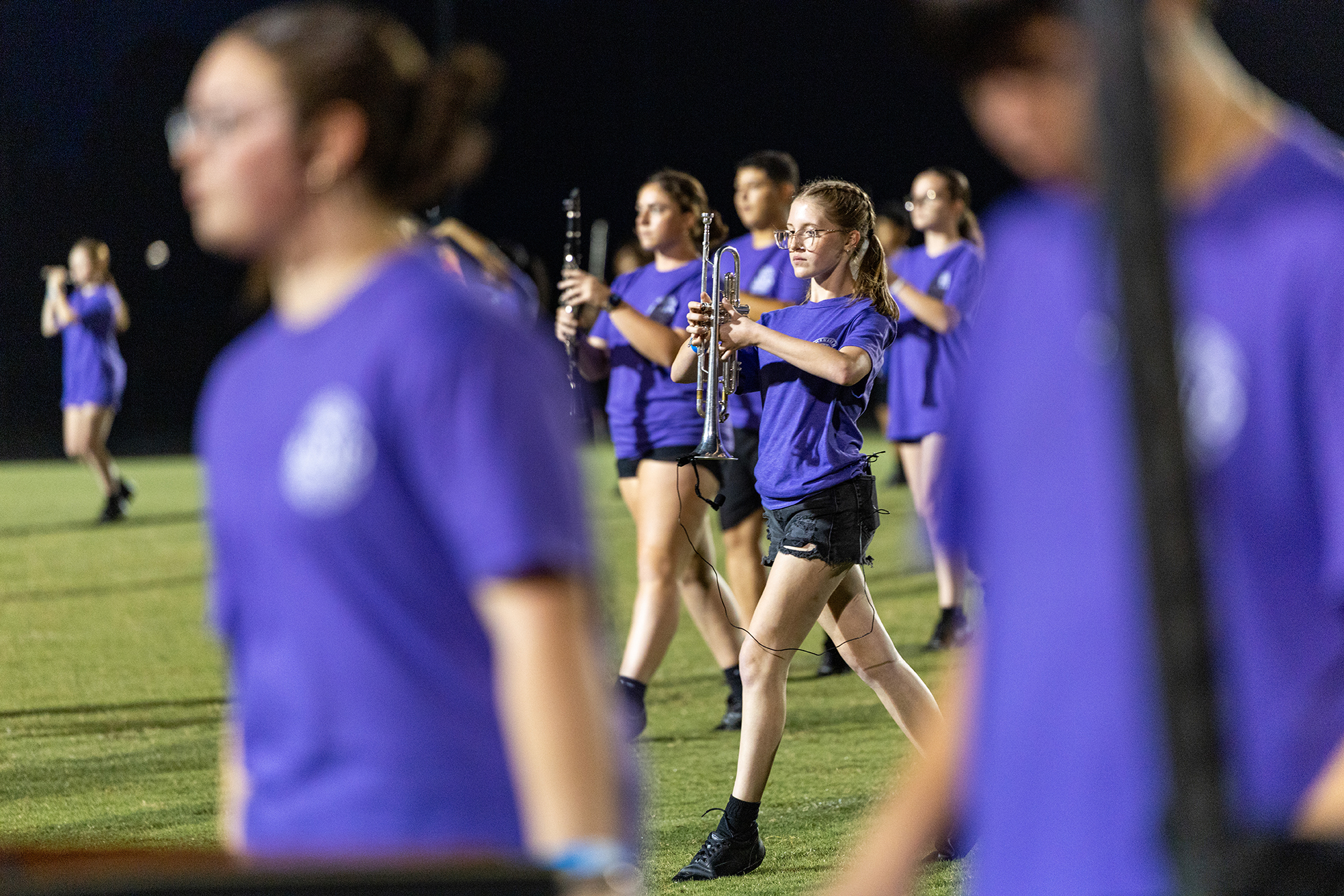 A group of people in purple uniforms practices on a field, one person walking in front.