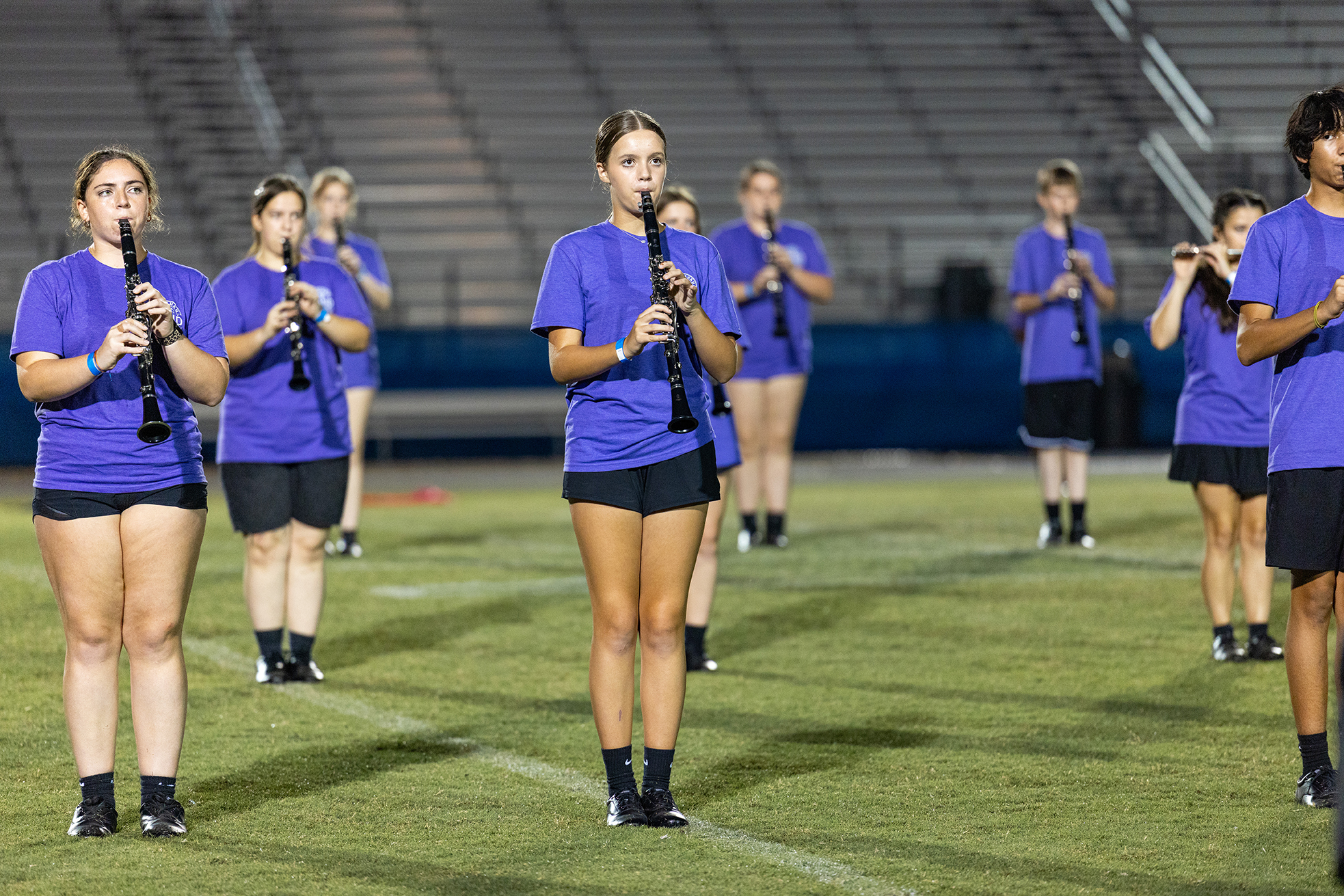 A group of musicians dressed in blue uniforms and black shorts play clarinets on a football field.