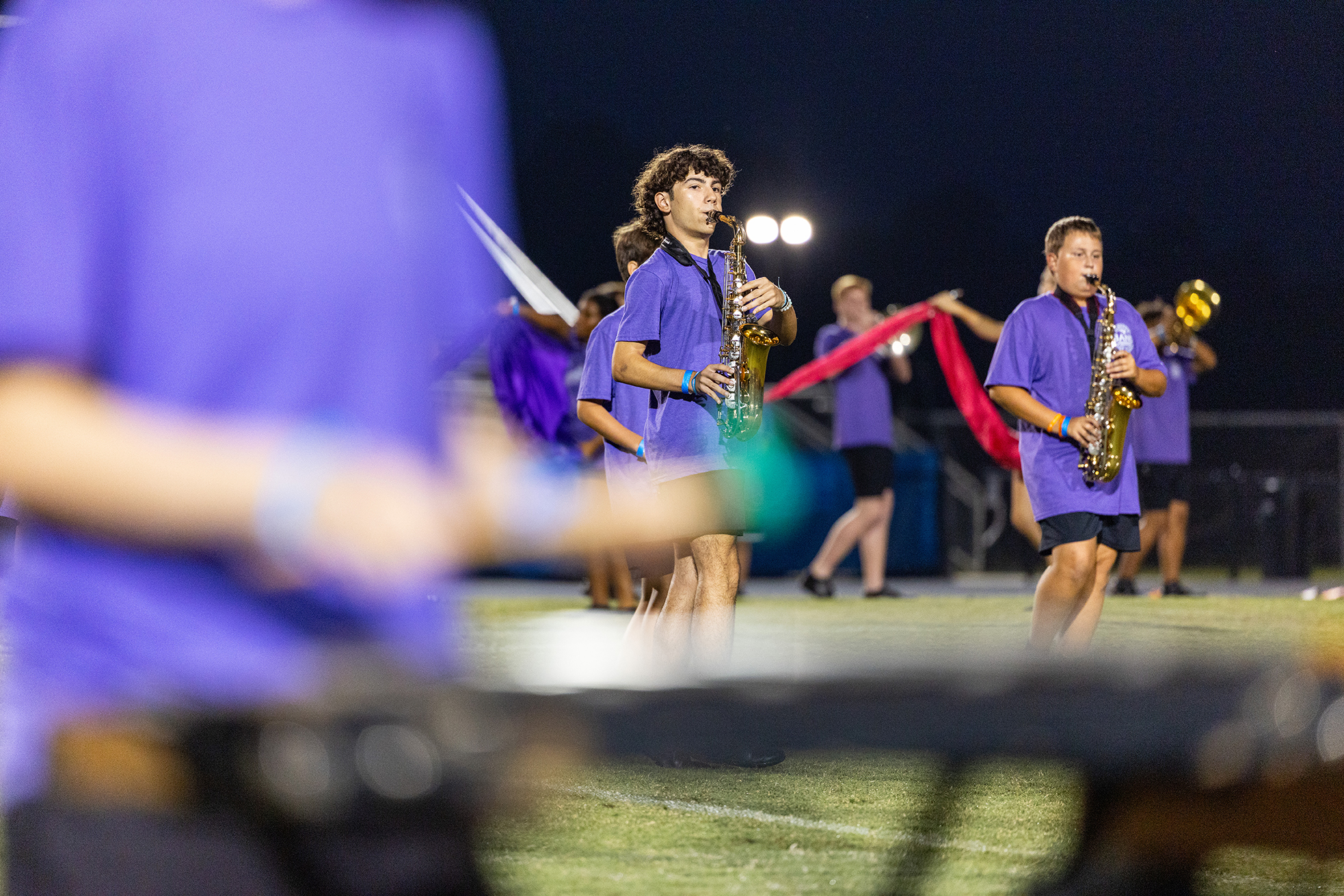 Several musicians play saxophones at an outdoor event. Two players are in the foreground, while others are blurred in the background.