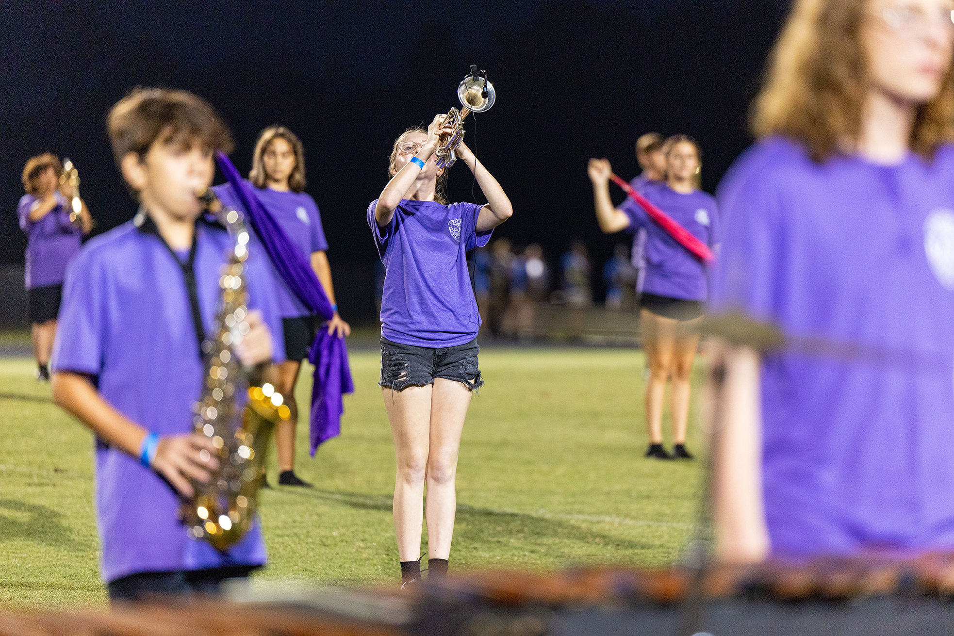 Group of students in purple uniforms performing on instruments at a school event at night.