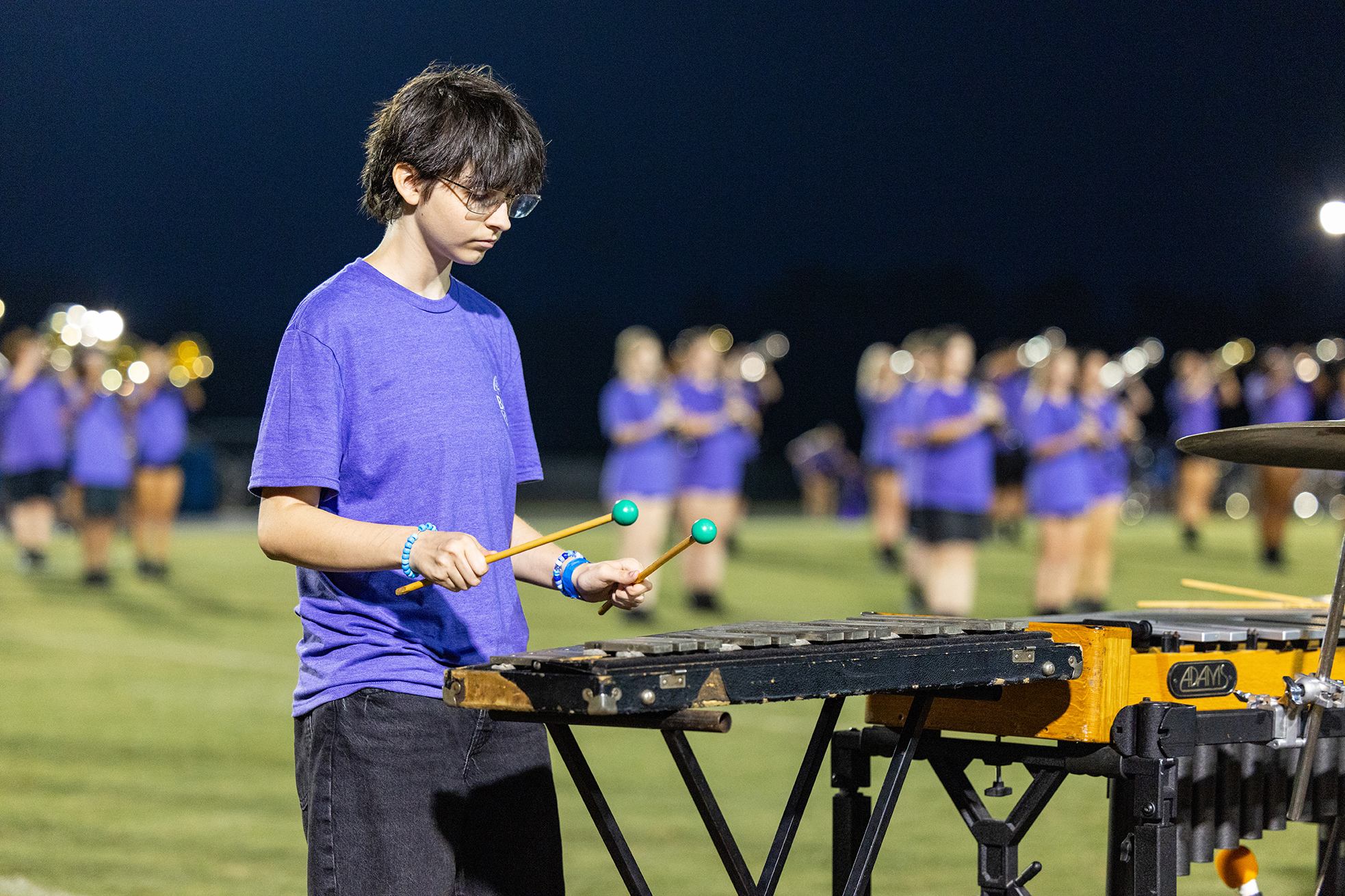 A child wearing a blue shirt and glasses plays a xylophone on a football field.