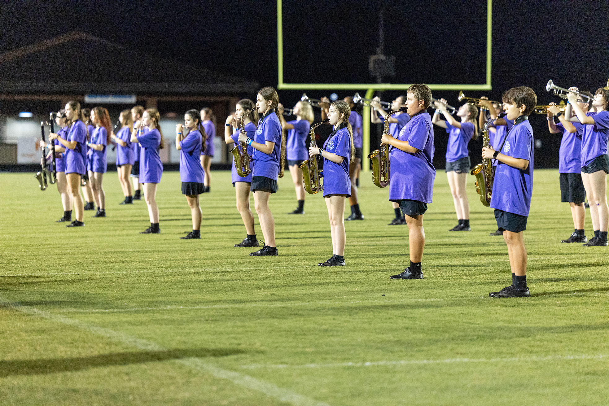A group of people in blue uniforms stand in a line on a field, playing trumpets.